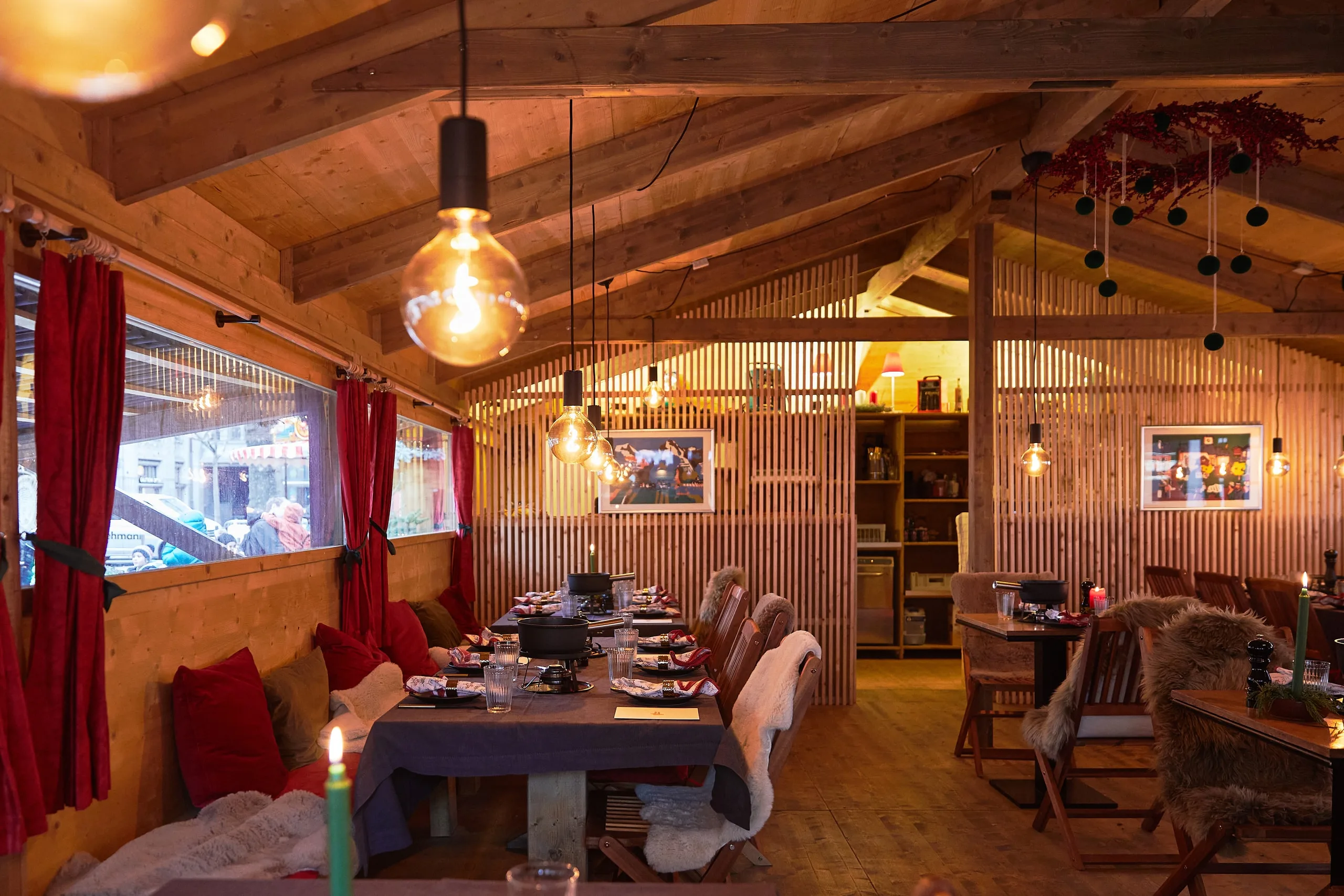 Fondue Chalet Zürich von innen: Holzchalet mit langer, gedeckter Tafel, Caquelons, Kerzen und Glühbirnen