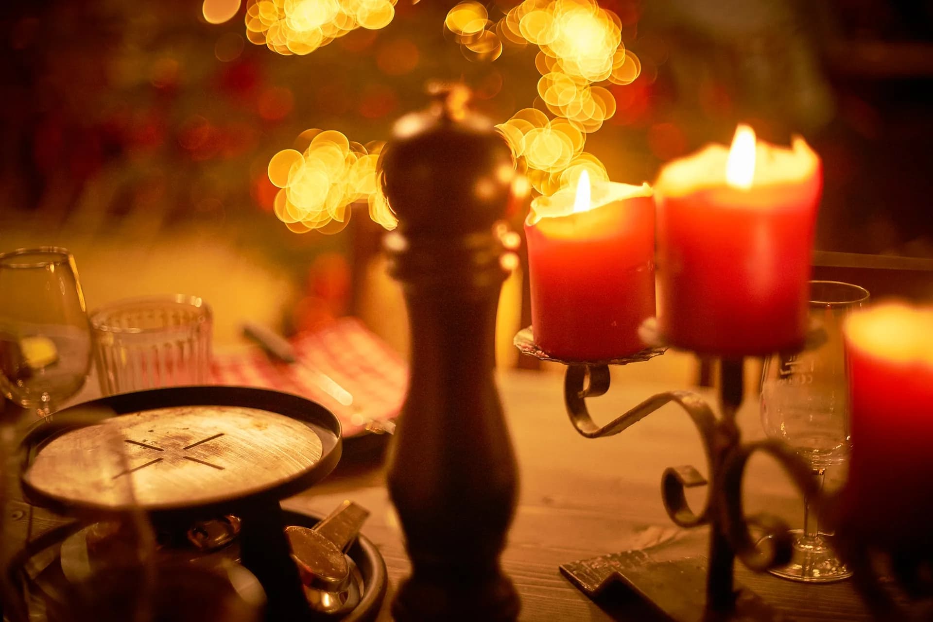 Rote Kerzen auf einem Kerzenständer und eine Pfeffermühle auf dem Tisch im Fondue Chalet, dahinter Lichterkette