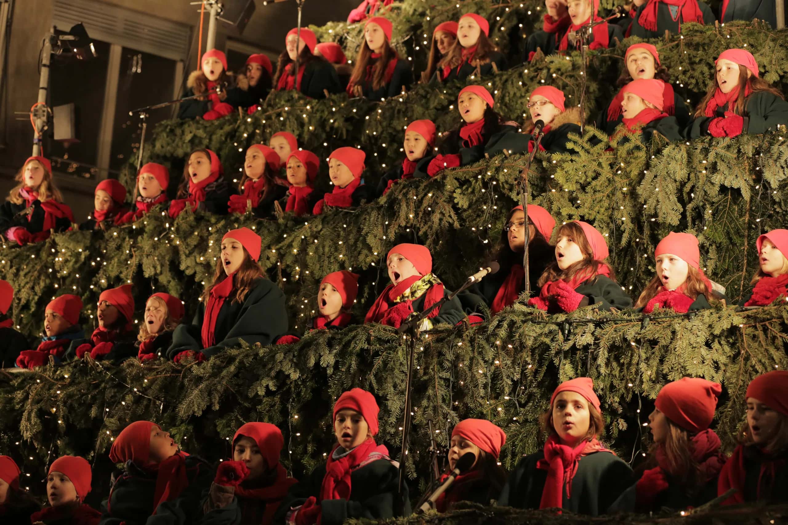 Kinderchor in roten Mützen und Schals singt auf den tannengeschmückten Stufen des Singing Christmas Tree in Zürich