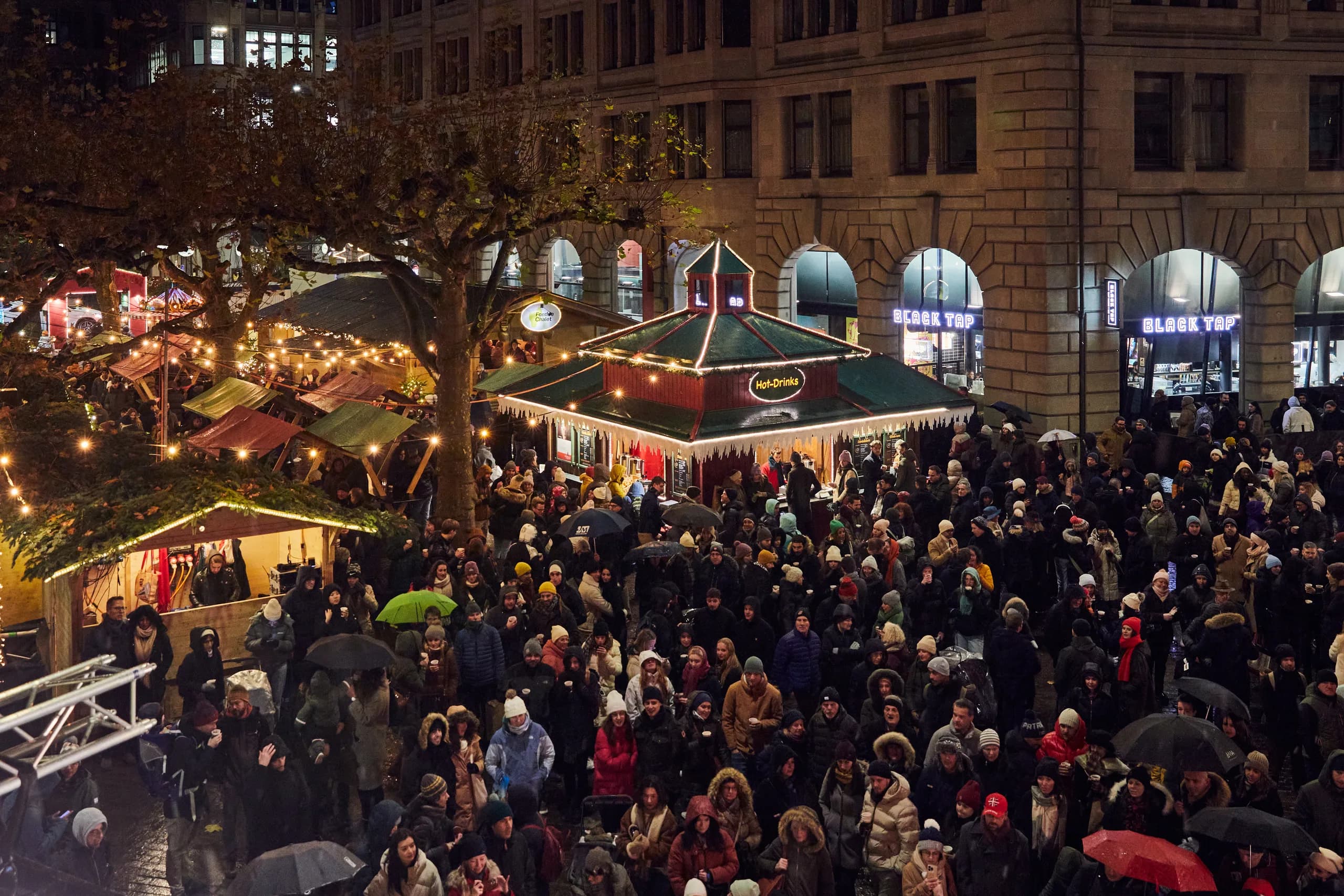 Blick von oben auf den Werdmühleplatz in Zürich: Publikum zwischen Hot-Drinks-Pavillon und beleuchteten Markthäuschen