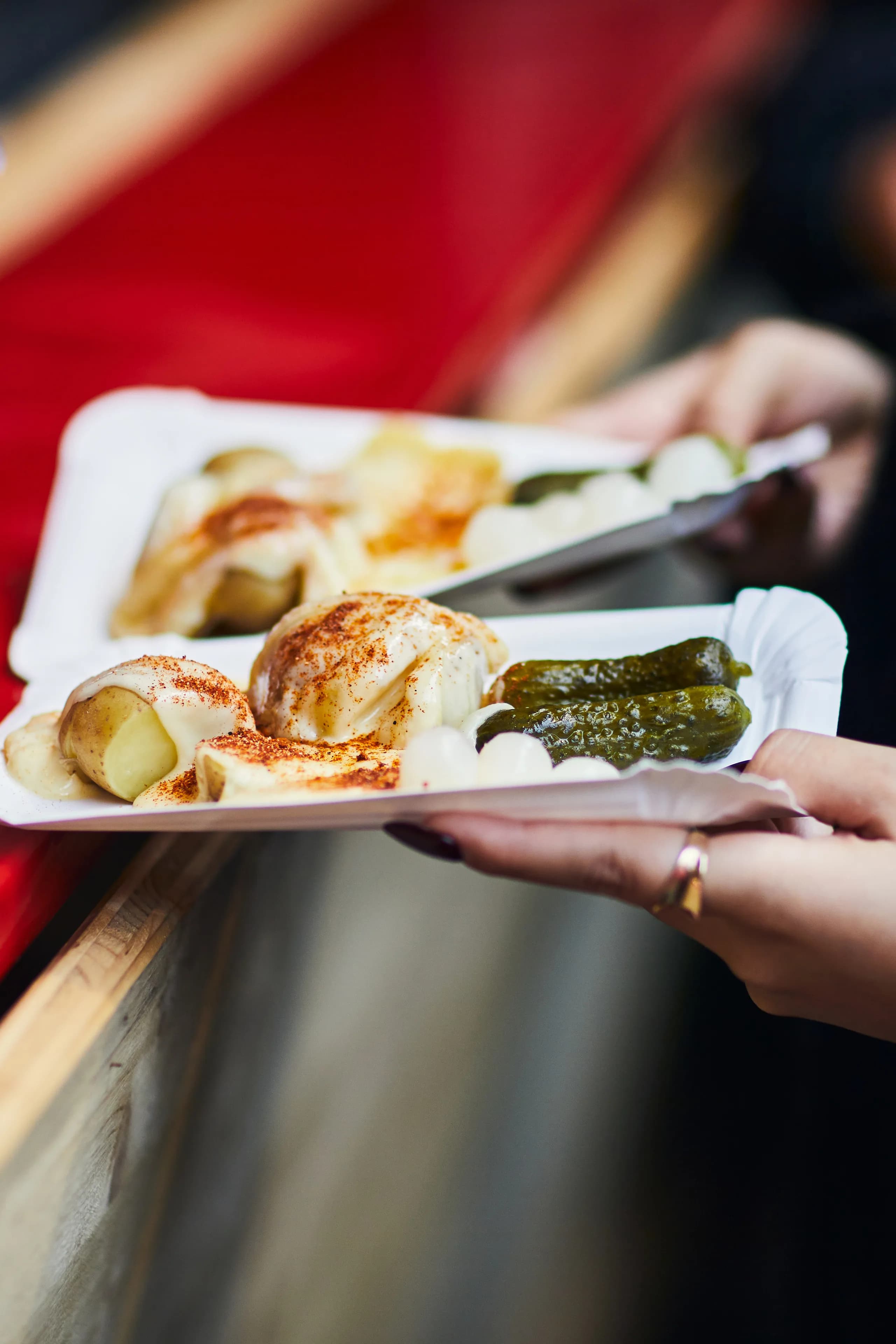 Raclette with potatoes, peppers, gherkins and pearl onions on cardboard plates, handed over the counter of a market stall
