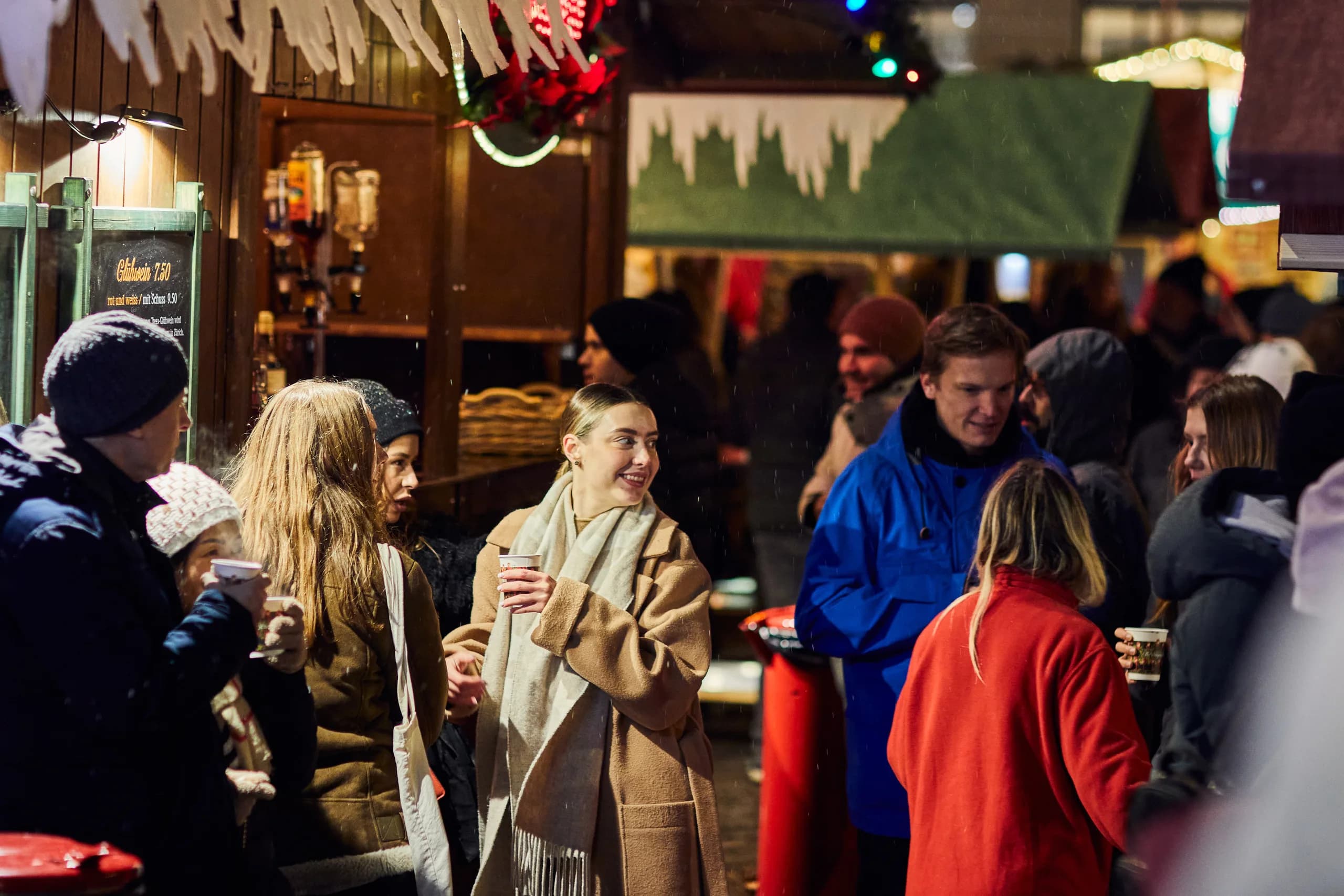 Young people with mulled wine cups chatting in front of a mulled wine stand at the Christmas market in the evening
